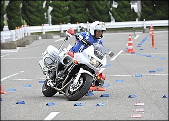 タイトコーナーへの進入場面。すでに車体は傾いているがブレーキレバーはまだかなり強く握りながら旋回動作へと移行している。熟練の白バイ隊員だからできるテクニックだ。