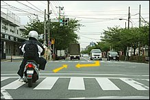 交差点で信号が青に変わるのを見計らって、左からすり抜けしてきたスクーターが飛び出してきました。対向車線の右折車は先に曲がってしまおうと焦っています。典型的な「右直事故」のパターンですよね。前方に駐車車両があるので、スクーターは急に車線変更してセンターに寄ってくるかもしれません。