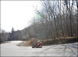 圧側ダンパーは中高速コーナーなど、旋回中に比較的高い荷重がかかるシーンで有効になります。圧側ダンパーを強めることで動的な高さを作っていくことも可能で、旋回中の適度な踏ん張り感やストロークに時間をかけられる、いわゆる「コシ感」を出すことが出来ます。逆に、雨天など滑りやすい路面では圧側をかけ過ぎるとスライドし易いので注意。