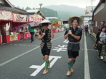 飯南町赤名に無事に着いて町民に拍手で迎えられる飛脚便。赤名は伊能忠敬が宿泊した宿場町でもある。丁度｢半夏まつり｣の真っ最中で多くの人出で賑わっている。